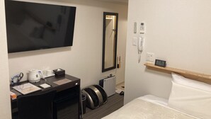 Et hotelværelse med en seng, et skrivebord med et fladskærms-tv, et spejl, en telefon og en lille hylde med et ur.