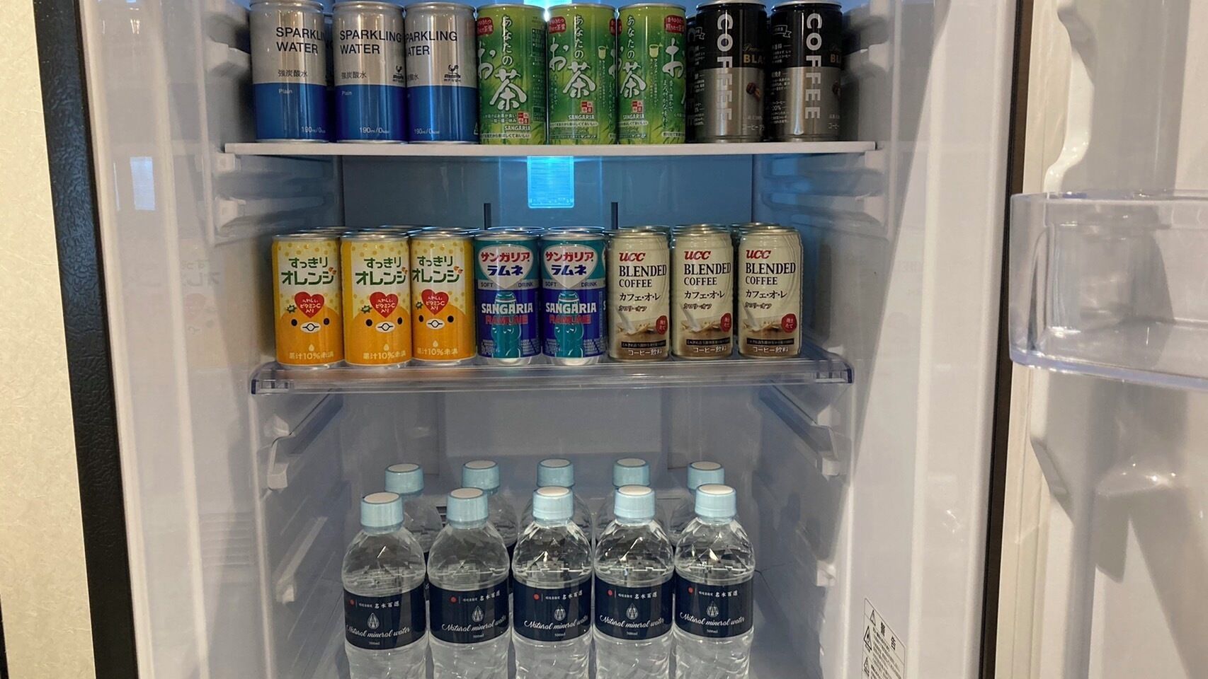 A refrigerator stocked with various beverages including sparkling water, coffee, and Sangaria drinks.