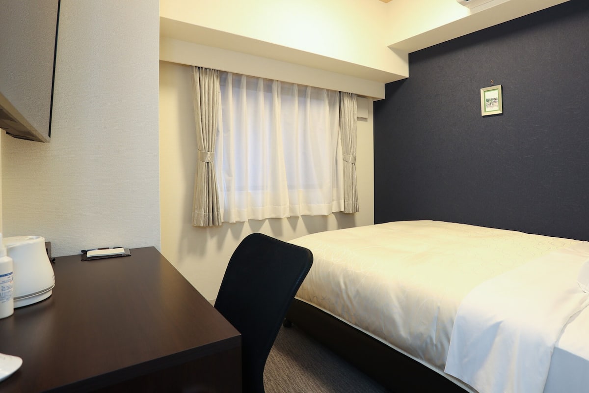 Ein Hotelzimmer mit einem Bett, einem Schreibtisch mit Telefon, einem Stuhl und einem Fenster mit Vorhängen.