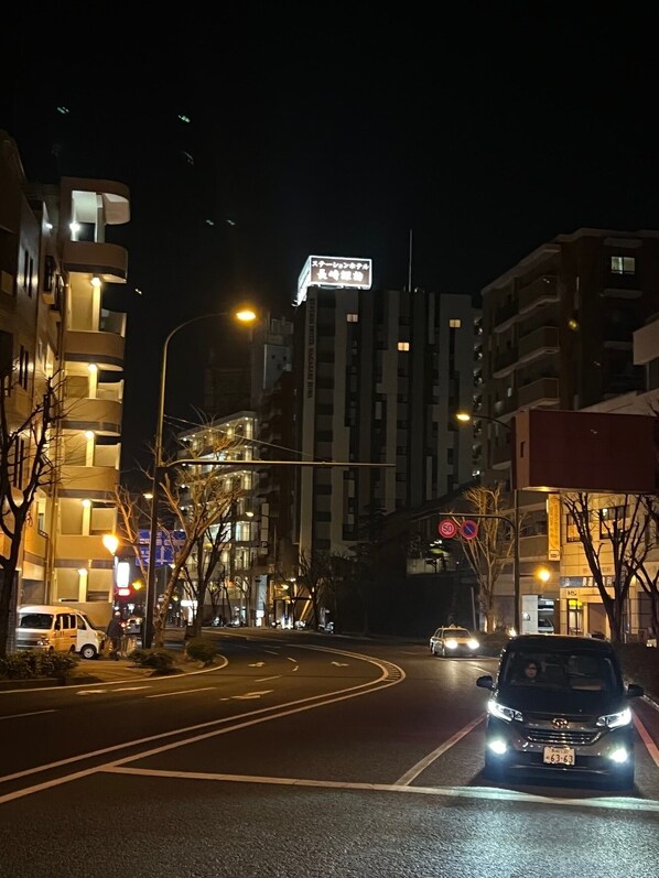 Una strada cittadina di notte, con palazzi, lampioni e un'automobile.