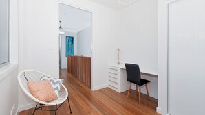 Un interior moderno con suelo de madera, una silla blanca con cojín, un escritorio con lámpara y un cuadro en la pared.