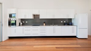 Una cocina moderna con gabinetes blancos, horno empotrado, microondas, hervidor y tostadora.