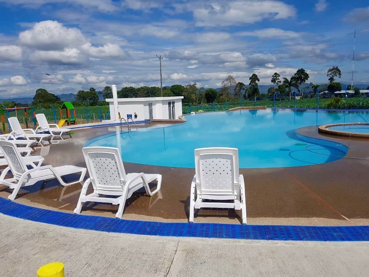 Ein Poolbereich mit Liegestühlen und einem kleinen Gebäude, umgeben von viel Grün.