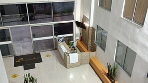 A modern hotel lobby with a reception desk, seating area, and large windows overlooking the street. - 5 km from the Coffee Park! - Montenegro LOFT with swimming pool in Quindio - (Montenegro)