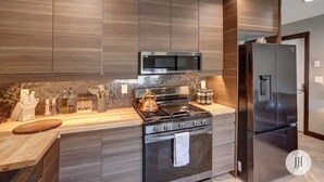 A modern kitchen with wood cabinetry, a stainless steel stove, a microwave, and a refrigerator. - Modern Luxurious Stay- Bidet- Lighted Mirror (Rapid City)
