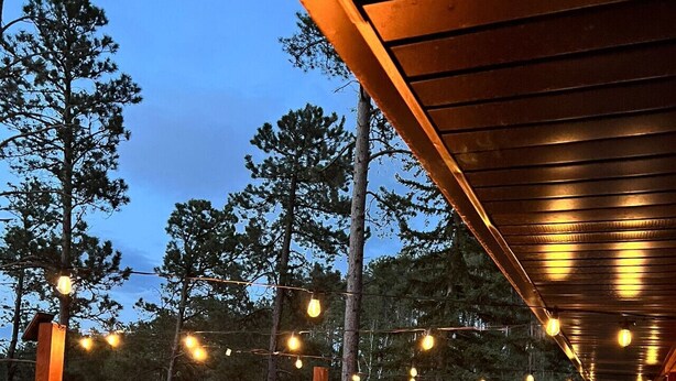 Un área de estar al aire libre con un brasero, luces colgantes y vistas al bosque.