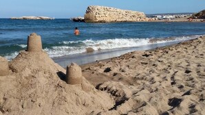 Una playa arenosa con formaciones rocosas y una persona en el agua.