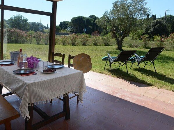 An outdoor dining area with a table set for two, chairs, and a view of a garden.