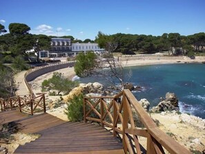 A wooden boardwalk leading to a beach with clear blue water, surrounded by rocky terrain and trees. - Charming ground floor house in Sant Martí d'Empúries HUTG-064209 (l'Escala)