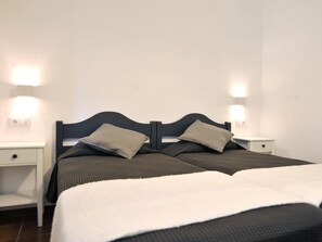 Una cama individual impecablemente hecha con dos almohadas, una mesita de noche y una lámpara de pared.