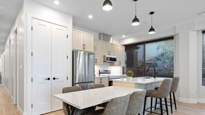 Une cuisine moderne dotée d’un îlot central, d’appareils électroménagers en acier inoxydable et d’un coin repas avec une table et des chaises blanches.