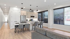 Une cuisine moderne dotée d’un îlot central, d’appareils électroménagers en acier inoxydable et de luminaires suspendus.
