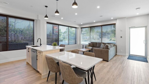 Une cuisine moderne dotée d’un îlot central, d’un coin repas avec des chaises et d’un espace détente avec un canapé et des coussins.