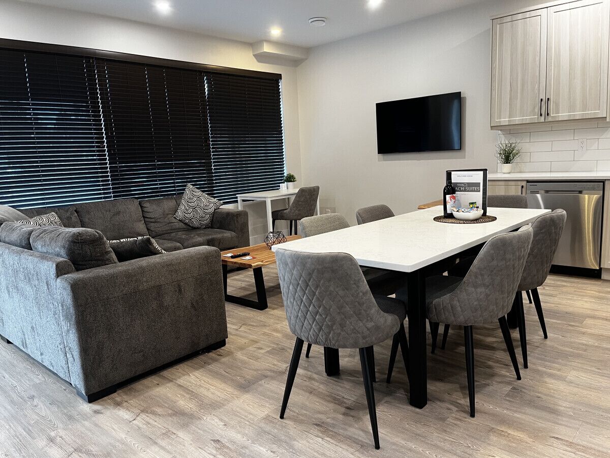 A modern living room with a sofa, chairs, a dining table, and a TV mounted on the wall.