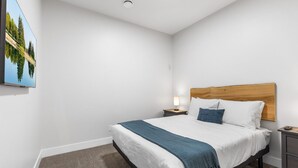 A bedroom with a bed, a nightstand, a wall-mounted TV, and a ceiling light. - 3-bedroom Daily Monthly Rates Available Unit 3 (Parksville)