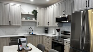 A modern kitchen with light wood cabinets, stainless steel appliances, a marble countertop, and a welcome book on the table. - 3-bedroom Daily Monthly Rates Available Unit 3 (Parksville)