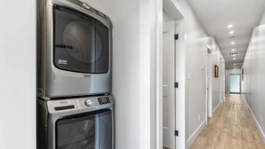 A laundry room with stacked appliances, a hallway with white walls and wooden flooring. - 3-bedroom Daily Monthly Rates Available Unit 3 (Parksville)