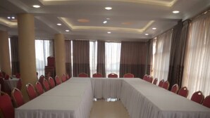 Un salón de conferencias con una larga mesa y sillas rojas, ventanas grandes con cortinas e iluminación empotrada en el techo.