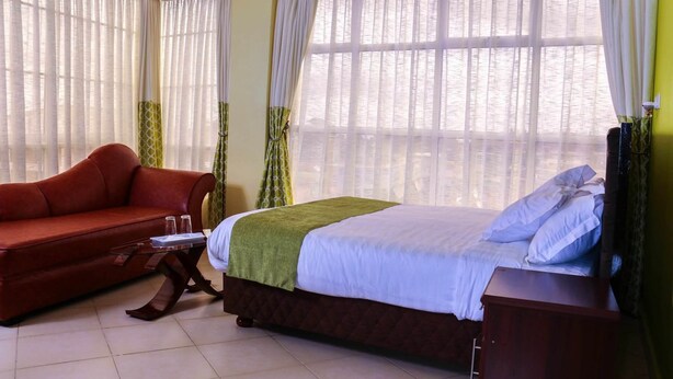 Una habitación de hotel con una cama, un sofá rojo, una mesita y cortinas.
