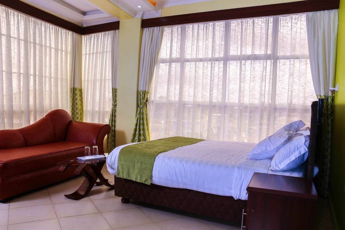 A hotel room with a bed, a red sofa, a small table, and curtains.