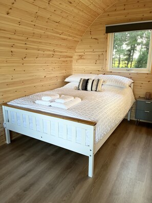 Dormitorio con paneles de madera, una cama, una mesita de noche y una ventana.