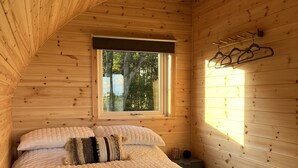 Un dormitorio acogedor tipo cabaña de madera con una cama, almohadas y una ventana.