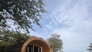 Una estructura de madera con techo curvo, puerta de vidrio y zona de estar con mesa y sillas.