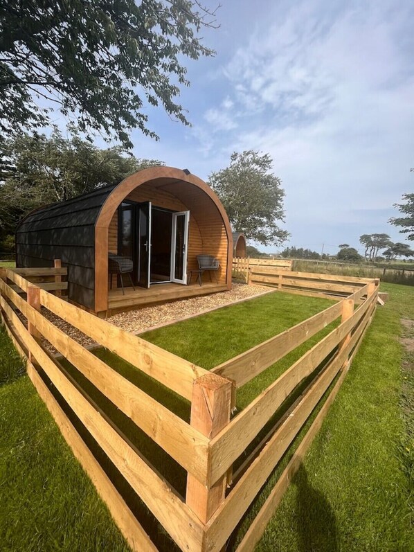 Una estructura de madera con techo curvo, puerta de vidrio y zona de estar con mesa y sillas.