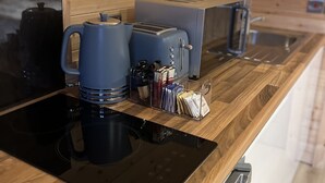 Cocina compacta con paredes de madera, placa de inducción negra, cafetera, tostadora y hervidor.