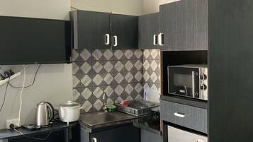 A compact kitchen with dark cabinets, a microwave, a kettle, and a small sink.