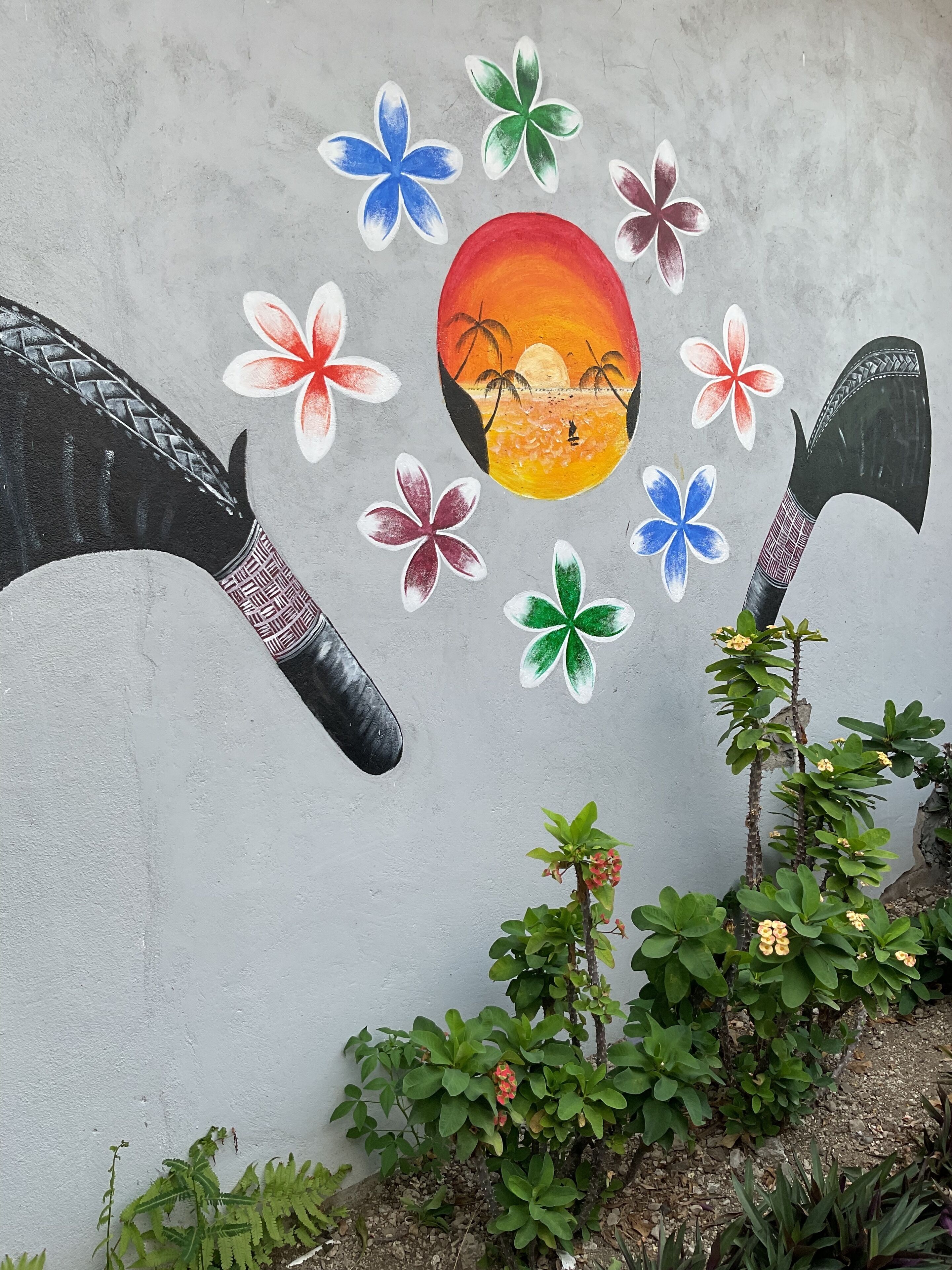 Pared con un mural de un atardecer, flores y dos hachas.