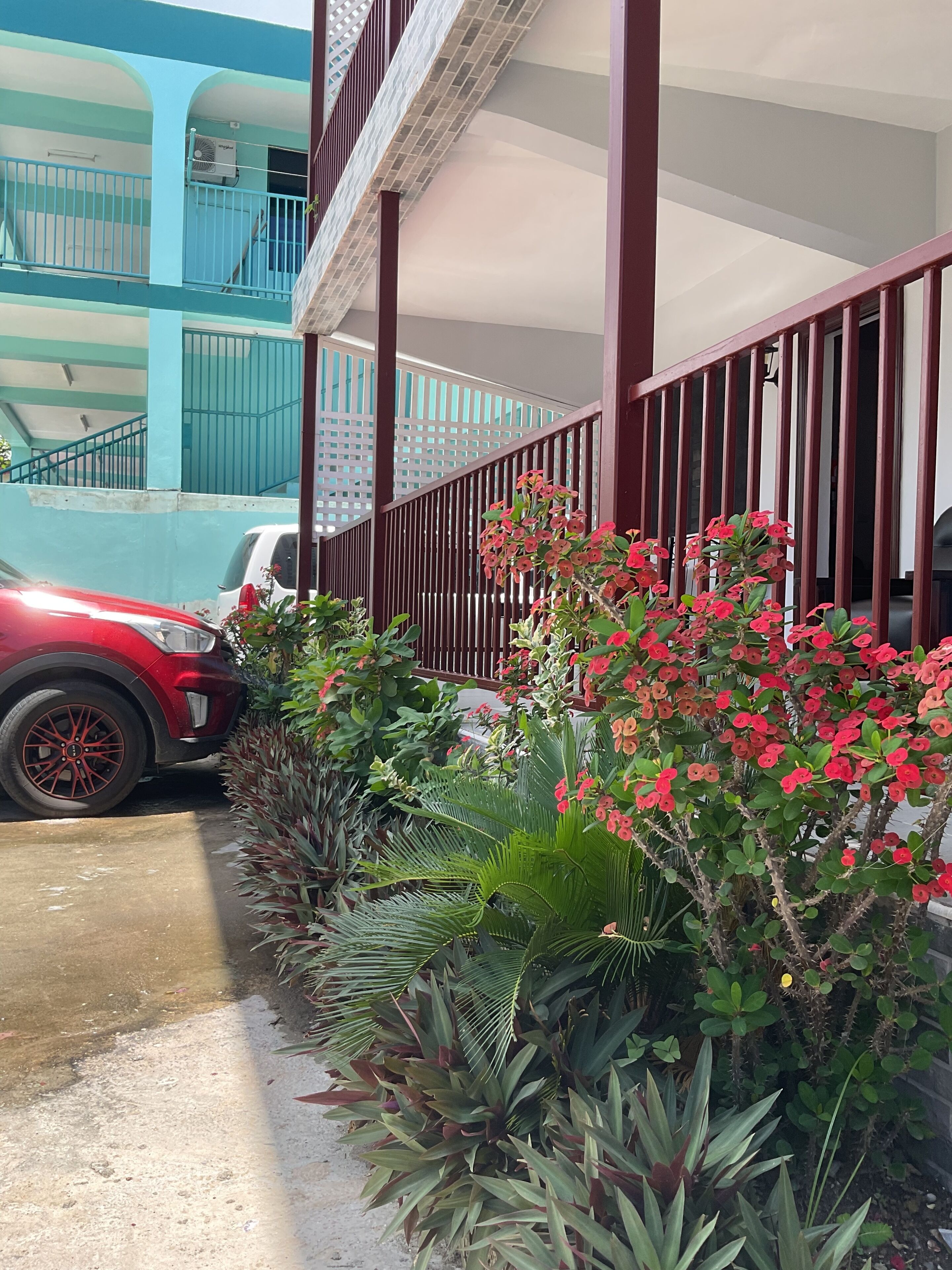 A red car parked in front of a building with a balcony and a staircase.