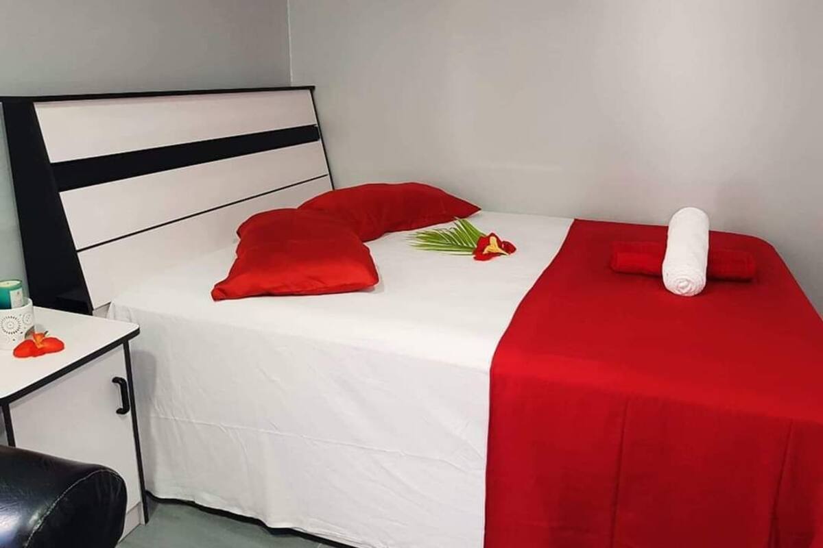 Un letto rifatto con una coperta bianca e rossa, un cuscino rosso e un asciugamano bianco arrotolato.