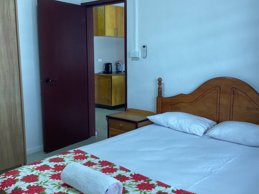 Habitación de hotel con cama, cabecera de madera, mesita de noche, pequeña mesa, armario y espejo.