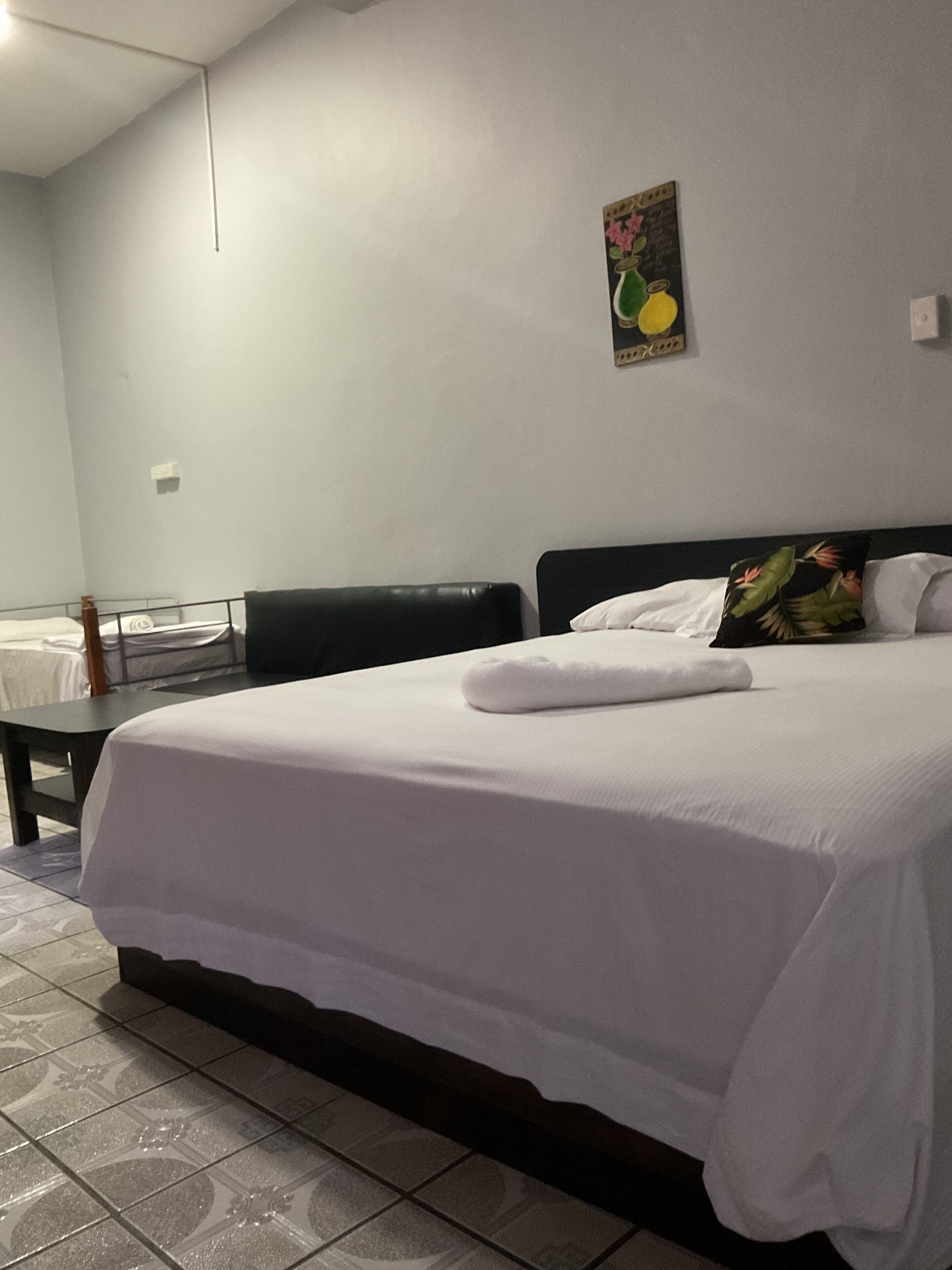 A hotel room with a large bed, a small table, and a wall-mounted painting.