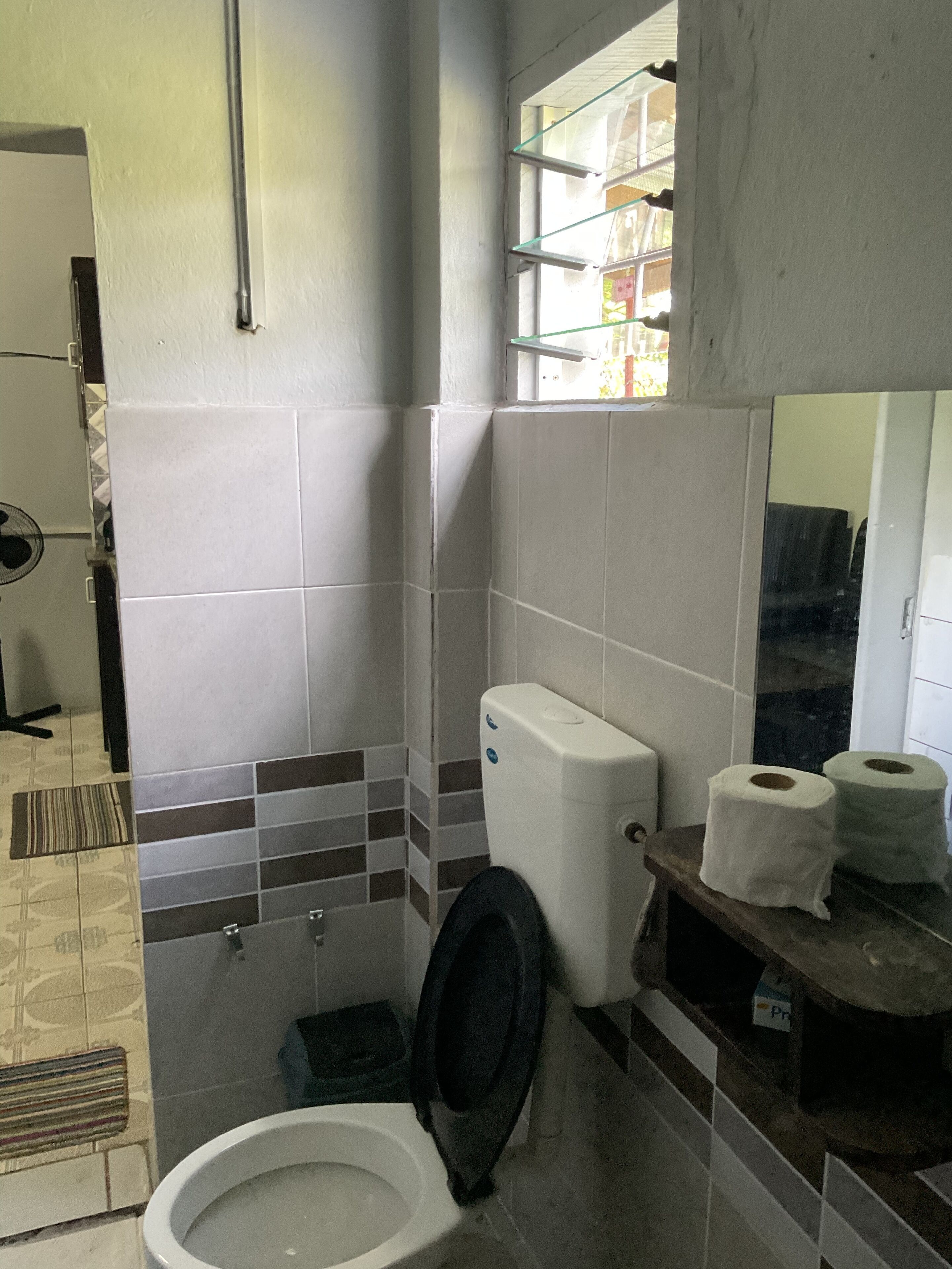 A bathroom with a toilet, a bidet, and a shelf with toilet paper.