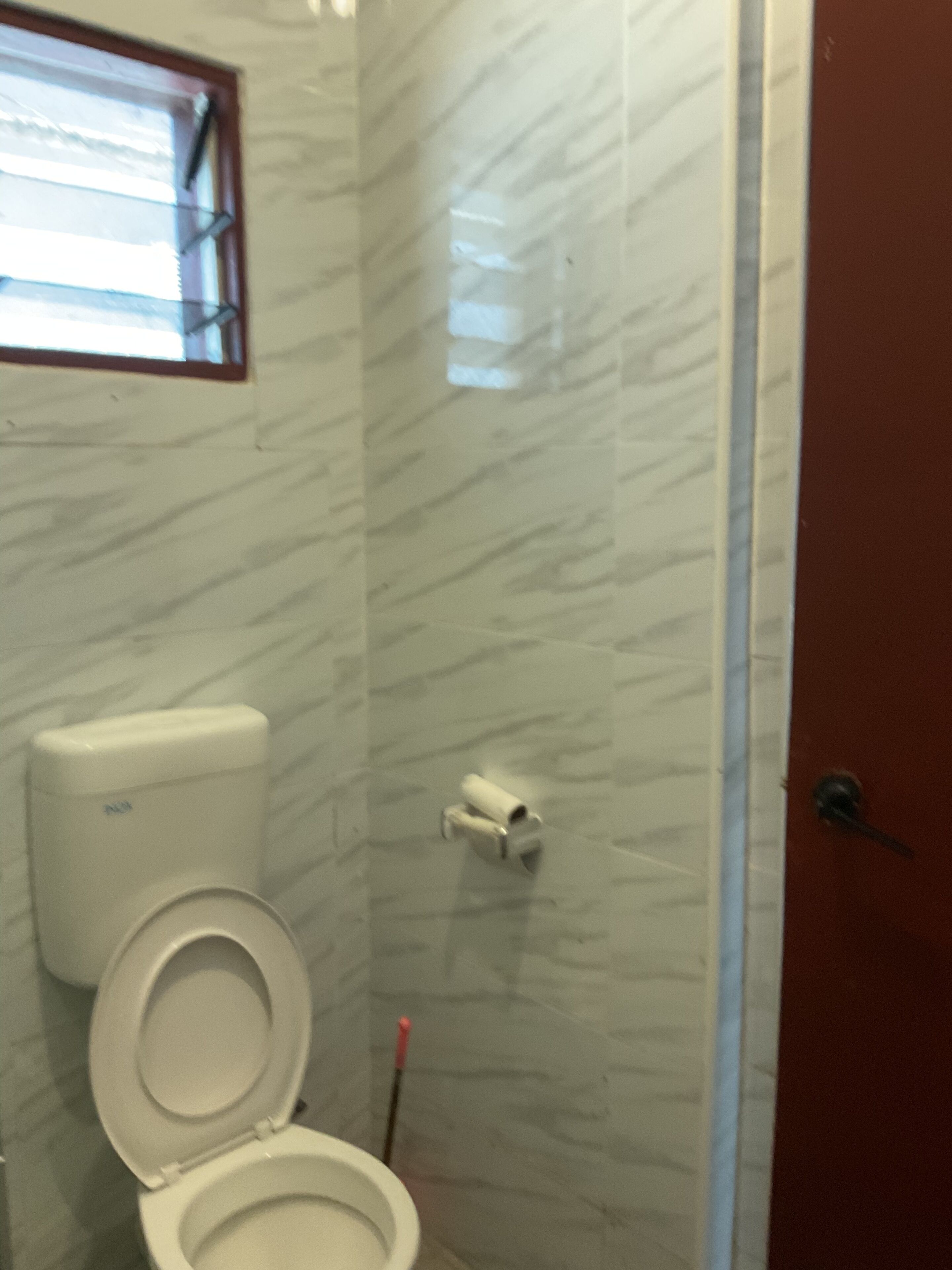 Un baño con inodoro, secamanos y un dispensador de papel higiénico en la pared.