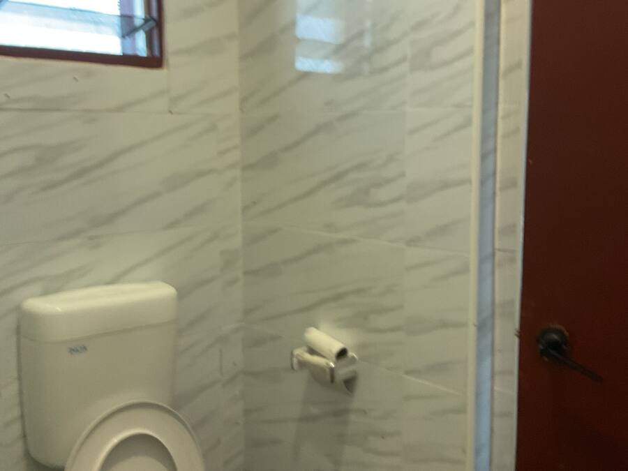 Un baño con inodoro, secamanos y un dispensador de papel higiénico en la pared.
