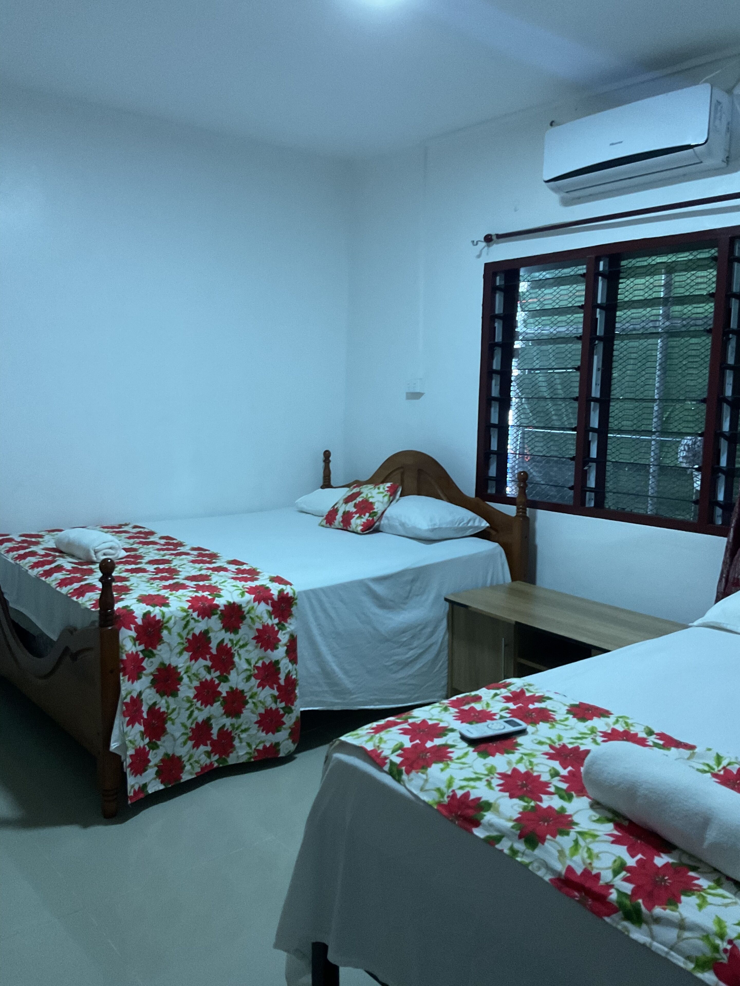 A room with two single beds, a wooden nightstand, a small table, and an air conditioning unit.