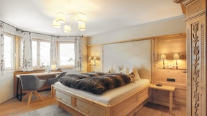 A bedroom with a bed, desk, and chair, wooden walls, and a window with curtains. - Appartement  Streifblick
Wohlfühlappartement für bis zu 6 Personen   (Kitzbühel)