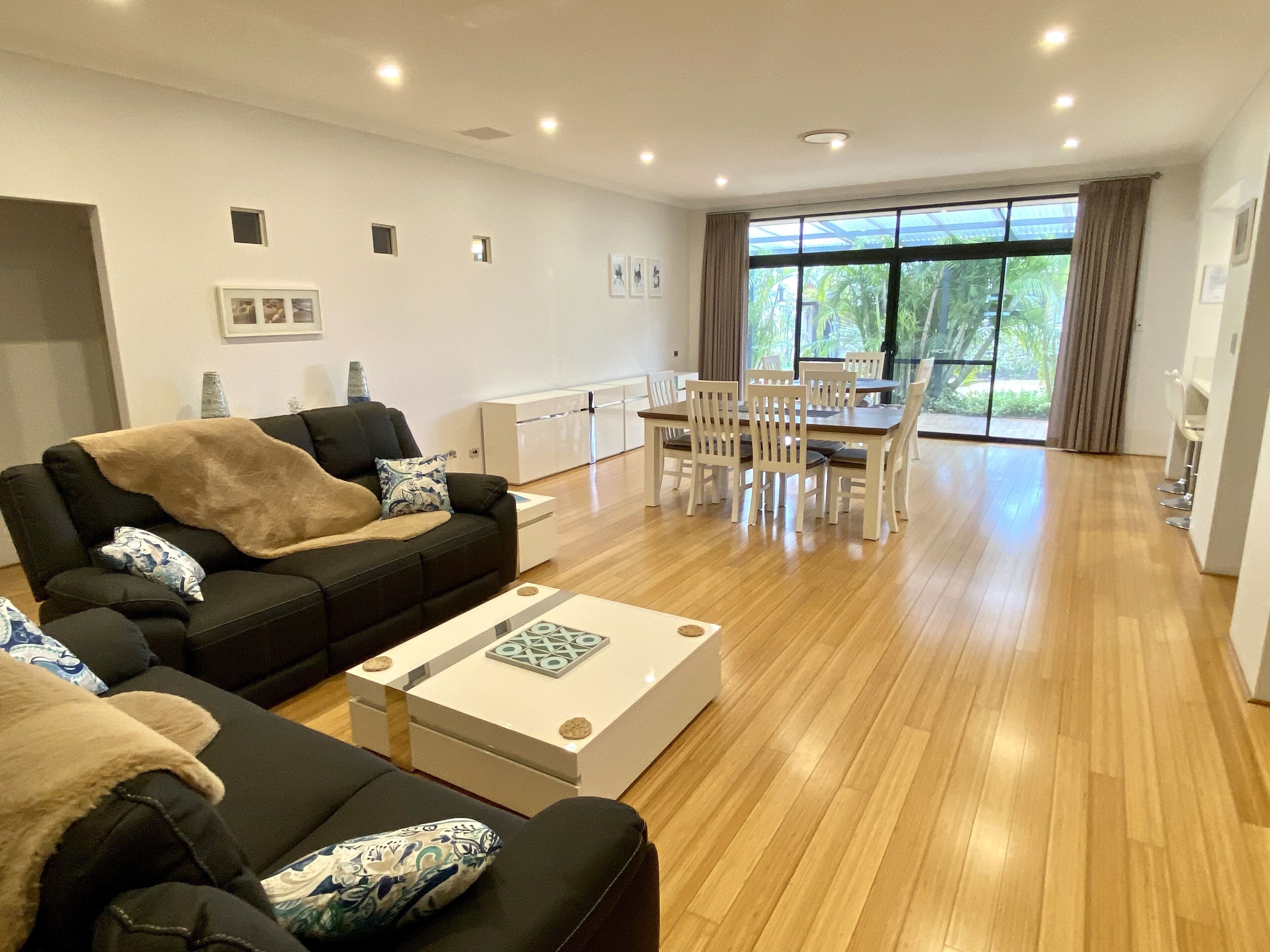 A spacious living room with a black sofa, a coffee table, and a dining area with white chairs and a table.