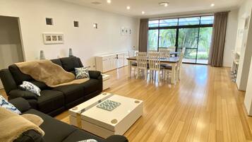 A spacious living room with a black sofa, a coffee table, and a dining area with white chairs and a table.