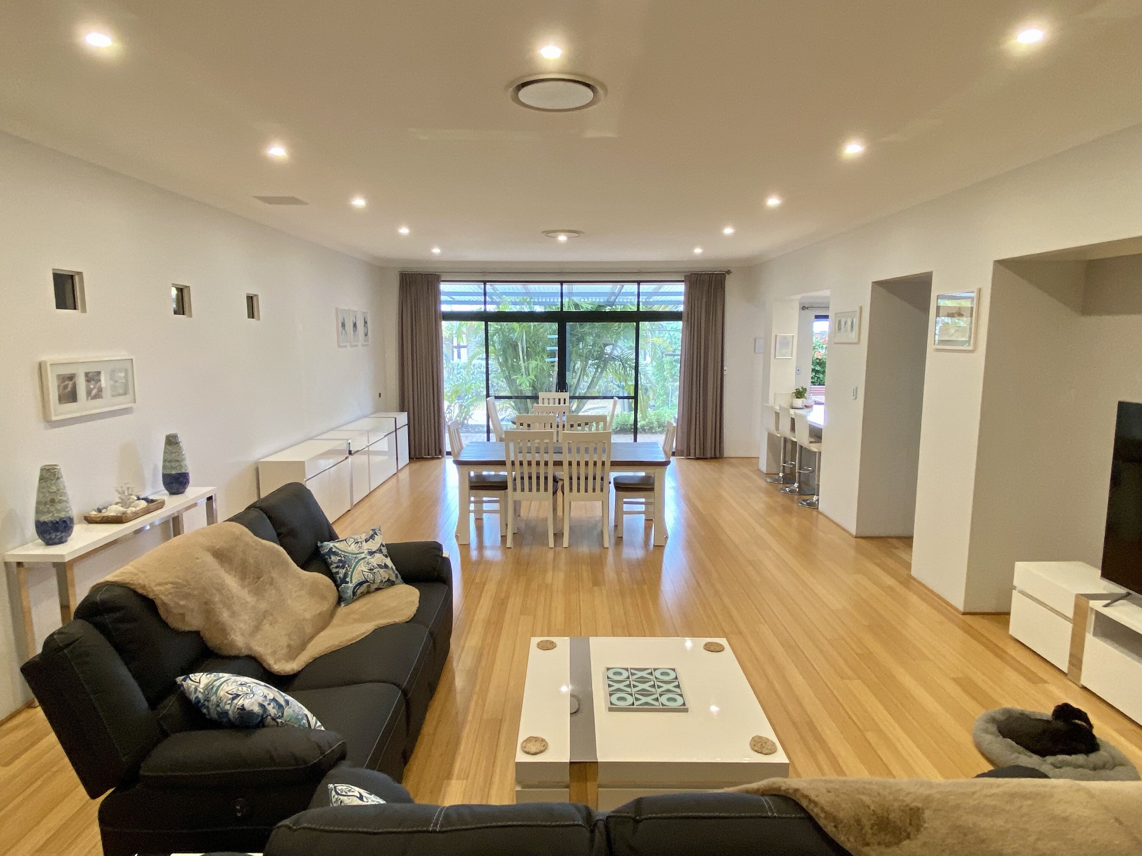 A modern living room with a black sofa, a coffee table, and a dining area with a white table and chairs.