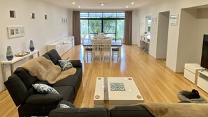 A modern living room with a black sofa, a coffee table, and a dining area with a white table and chairs. - Baudins Bed & Breakfast - Adults Only (West Busselton)