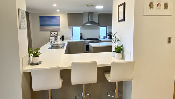 A modern kitchen with a central island, bar stools, and a view of the living area. - Baudins Bed & Breakfast - Adults Only (West Busselton)