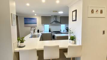 A modern kitchen with a central island, bar stools, and a view of the living area.