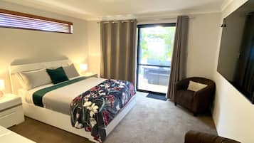 A hotel room with a bed, a chair, a desk, and a large window with curtains.