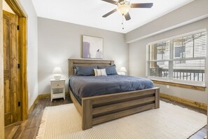Un dormitorio con cama de madera, lámparas de noche, ventilador de techo, ventana con persianas y una puerta.