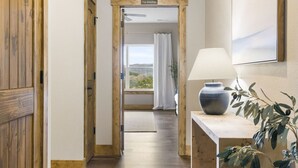 Un pasillo con puertas de madera, un cartel que dice 'The Masters', una ventana con vistas y una lámpara sobre una mesa de madera.