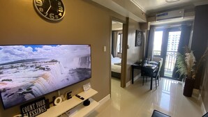 A modern living room with a flat-screen TV displaying a waterfall scene, a clock, and a sign that reads "COUNT YOUR BLESSINGS". - 1 BR Fully Furnished Condo Across MOA with Pool and Parking - S Res. Unit 0916 (Pasay)